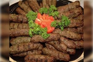 Travessa com kaftas douradas e suculentas recém-saídas do forno, com vapor subindo. Fundo rústico com utensílios de cozinha ao redor, criando um clima acolhedor