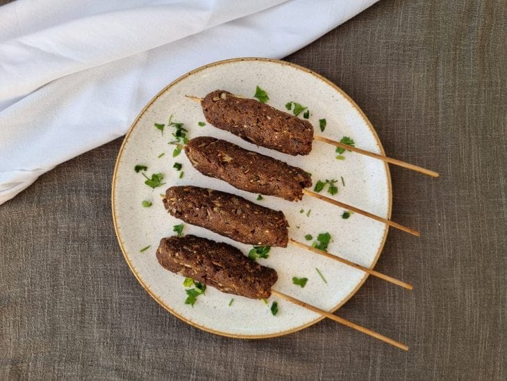 Travessa com kaftas douradas e suculentas recém-saídas do forno, com vapor subindo. Fundo rústico com utensílios de cozinha ao redor, criando um clima acolhedor