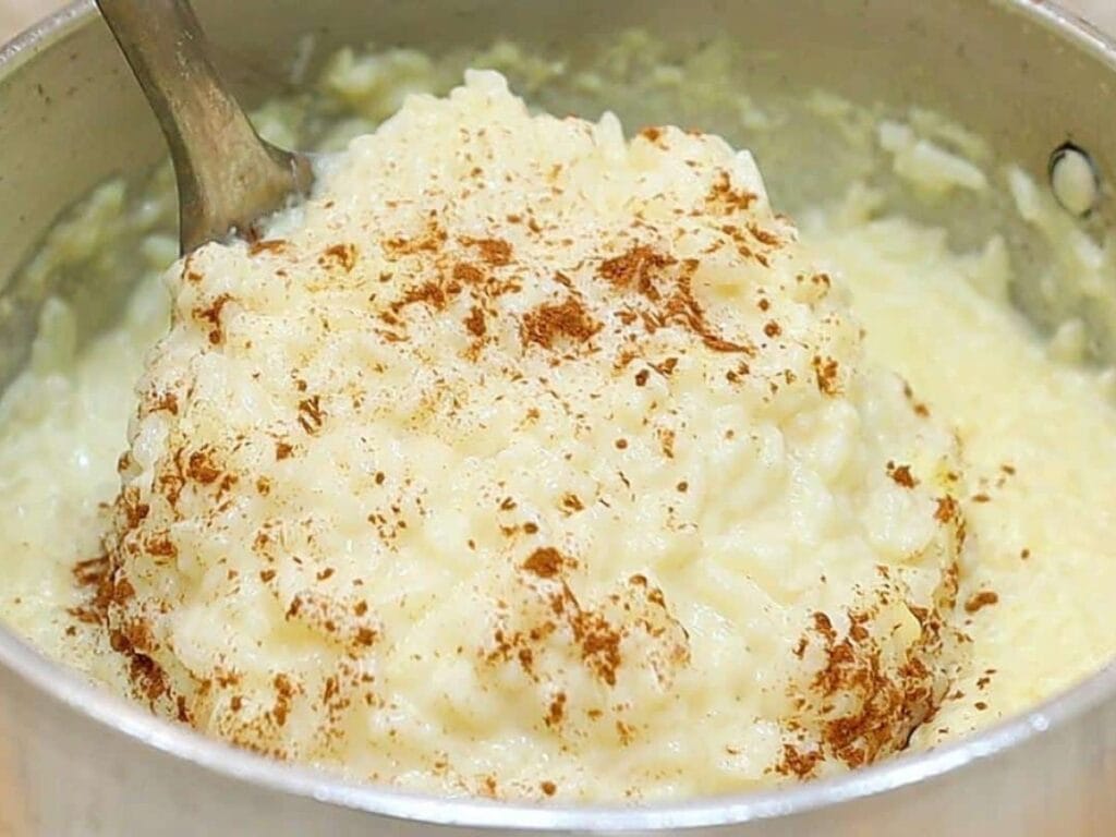 Tigela de arroz doce cremoso, polvilhado com canela em pó e decorado com um pau de canela.