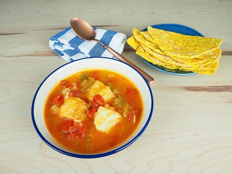 Bacalhau ensopado com batatas, cebolas, tomates e pimentão em caldo aromático, sendo cozido em uma panela grande.