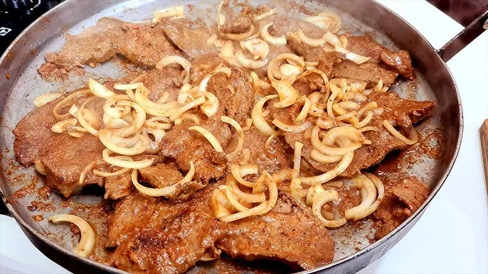 Prato com bife de fígado acebolado, coberto com cebolas caramelizadas e salsinha fresca.