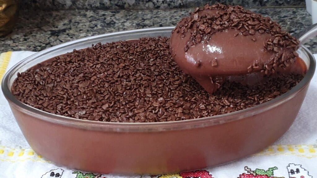 Brigadeiros enrolados e passados em chocolate granulado, com um brigadeiro de colher ao fundo, mostrando a textura cremosa.