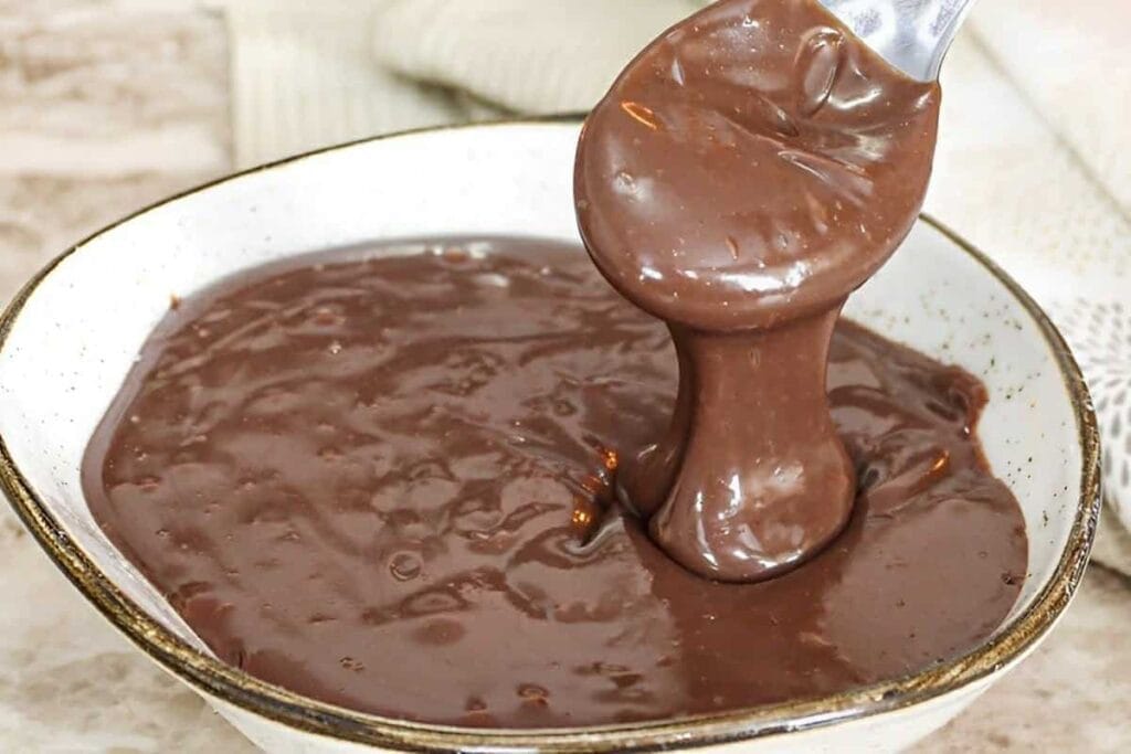 Brigadeiros enrolados e passados em chocolate granulado, com um brigadeiro de colher ao fundo, mostrando a textura cremosa.