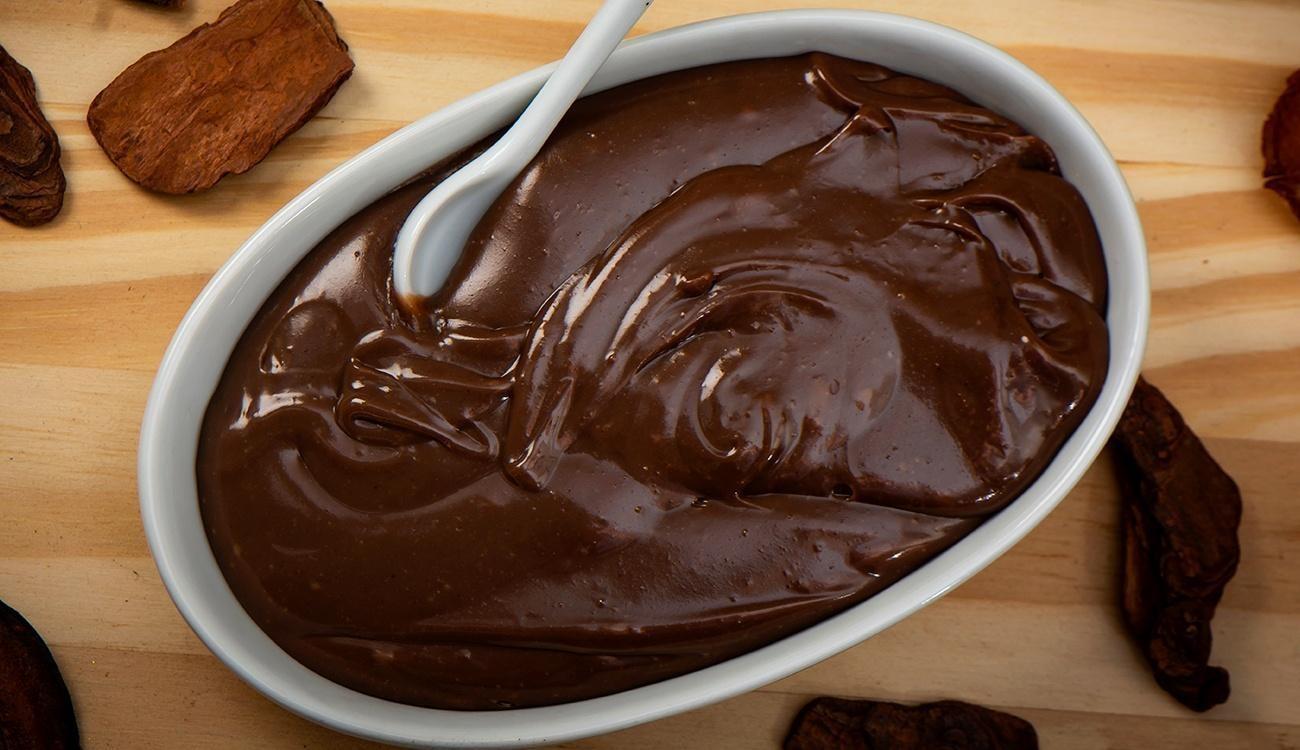 Brigadeiros enrolados e passados em chocolate granulado, com um brigadeiro de colher ao fundo, mostrando a textura cremosa.