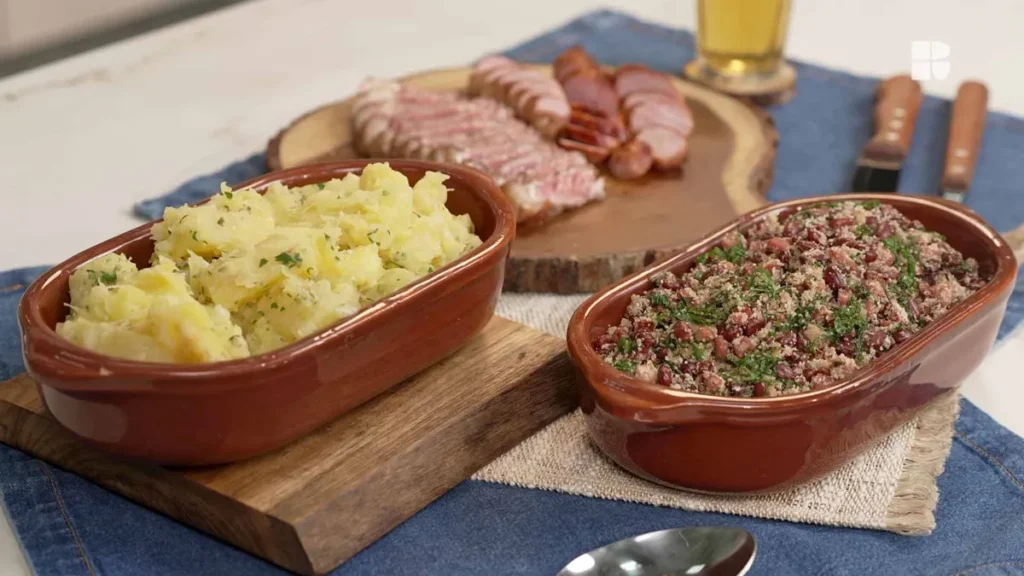 Feijão tropeiro servido como acompanhamento para churrasco, com bacon crocante, ovos cozidos e farofa de mandioca, em uma mesa decorada para um evento familiar.