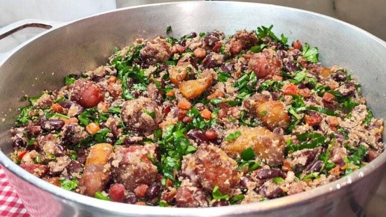 Prato de feijão tropeiro com carne grelhada ao fundo, mostrando uma refeição típica de churrasco brasileiro, com ingredientes frescos e saborosos.