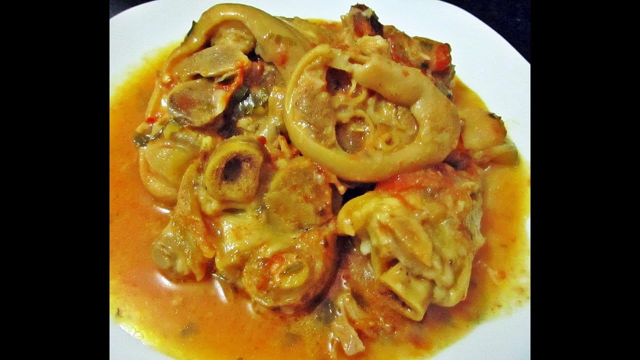 Pés de porco cozidos em uma travessa, com caldo e cheiro-verde picado.