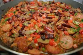 Panela grande com entrevero, mostrando pedaços de carne bovina, frango, linguiça, batata, cenoura e pimentões coloridos.