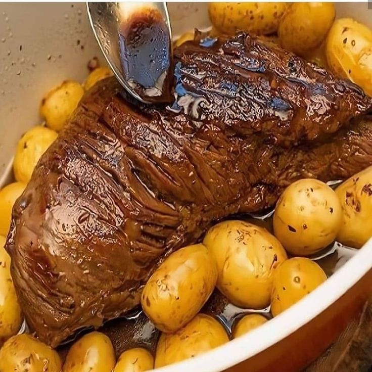 Maminha na cerveja preta fatiada em uma travessa, regada com o molho escuro e brilhante do cozimento, ao lado de um ramo de alecrim.