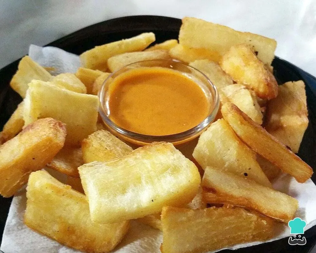 Porção de mandioca frita passada no ovo, dourada e crocante, servida em um prato com fatias de limão.