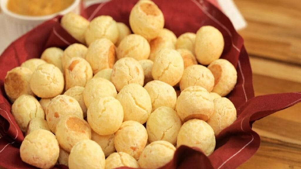 Pães de queijo dourados e macios, servidos em uma cesta com uma xícara de café ao lado.