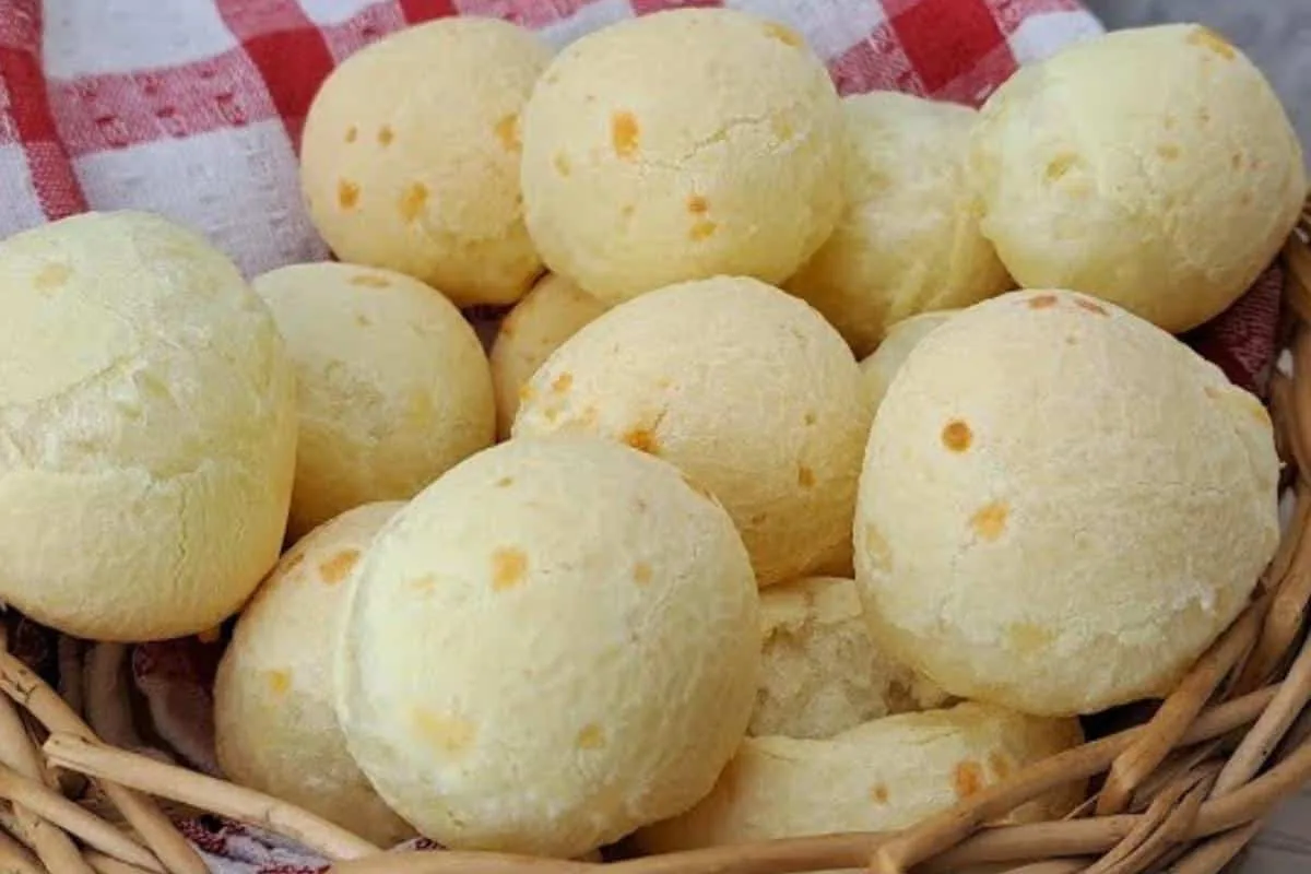 Pães de queijo dourados e macios, servidos em uma cesta com uma xícara de café ao lado.