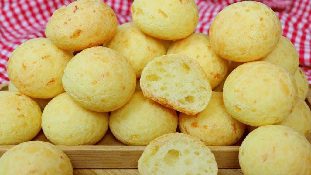 Pães de queijo dourados e macios, servidos em uma cesta com uma xícara de café ao lado.