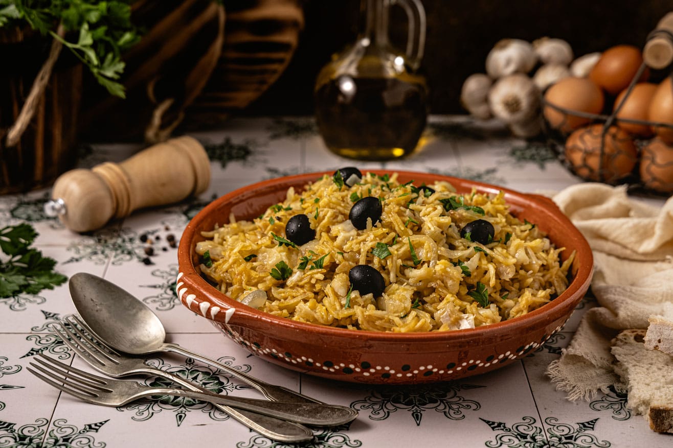 Bacalhau à Brás servido em uma travessa, decorado com azeitonas pretas e salsinha fresca.