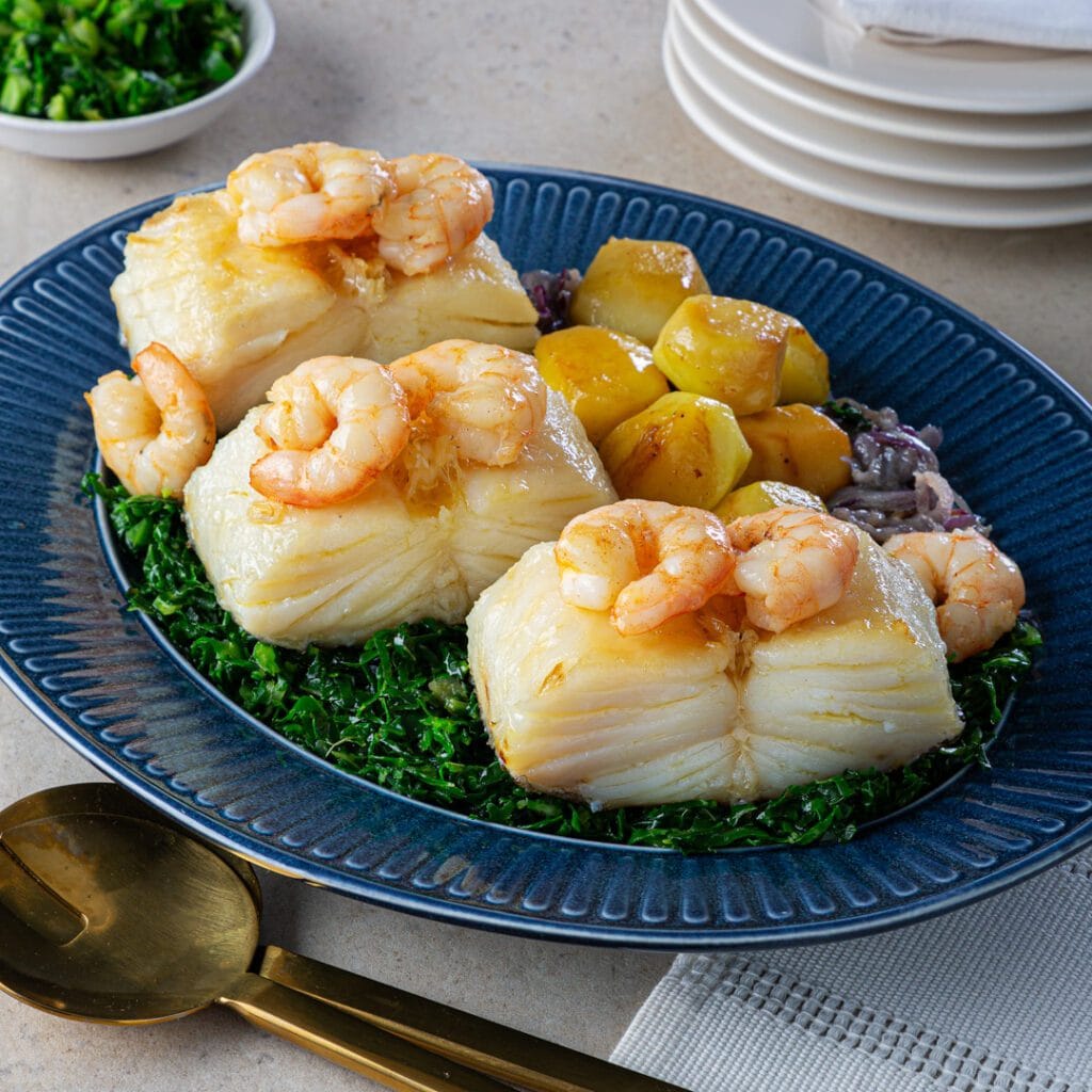 Bacalhau com camarão servido em uma travessa, com batatas cozidas, pimentão e salsinha fresca, regado com azeite de oliva.