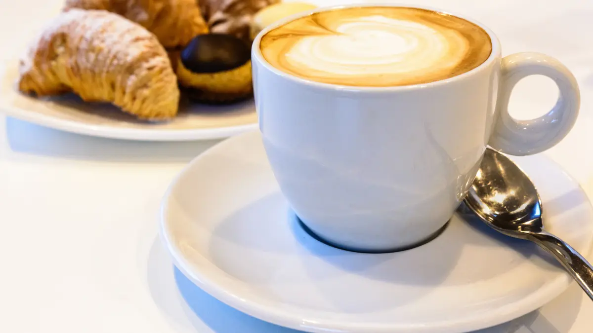 Xícara de cappuccino cremoso com espuma de leite por cima, polvilhado com cacau em pó.