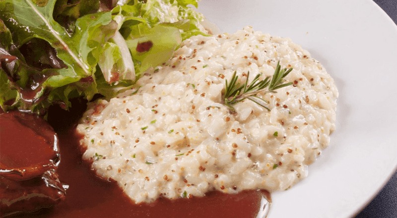 Um prato de arroz à piamontese cremoso, servido ao lado de um bife grelhado, representando uma das combinações sugeridas no artigo.