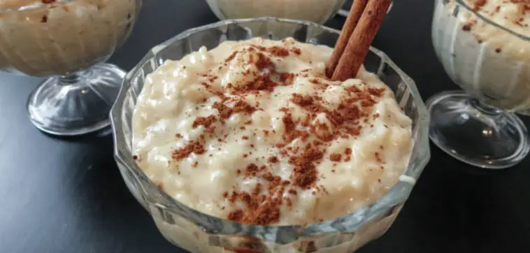 Tigela de arroz doce cremoso, com creme de leite, polvilhado com canela em pó e decorado com um pau de canela.