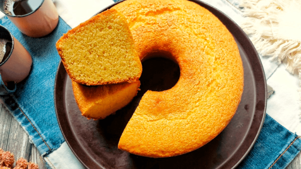 Um bolo de fubá fofinho e dourado, com pedaços de goiabada derretendo no interior e uma fatia generosa servida em um prato, representando o resultado final da receita e a tentação desse bolo clássico.