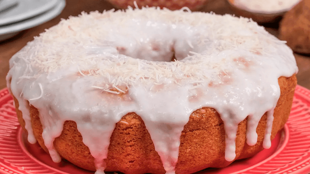 Bolo de coco fofinho com calda cremosa de coco escorrendo, coco ralado polvilhado por cima.