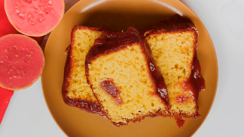 Foto apetitosa de um bolo de goiaba fresca de liquidificador recém-assado e fofinho, decorado com goiabas frescas e açúcar de confeiteiro.