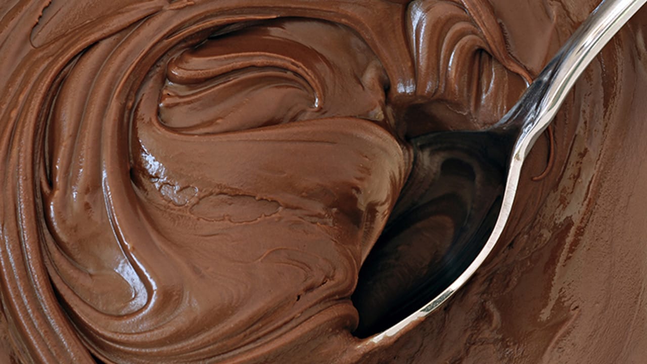 Brigadeiros enrolados e passados em chocolate granulado, e um brigadeiro de colher em uma colher, mostrando a textura cremosa.