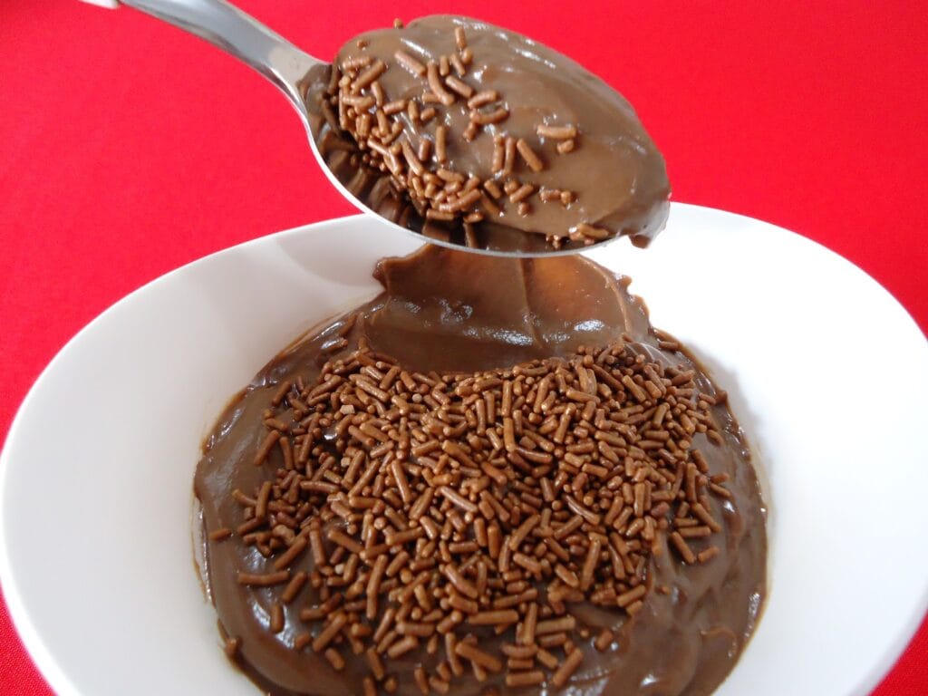 Brigadeiros enrolados e passados em chocolate granulado, e um brigadeiro de colher em uma colher, mostrando a textura cremosa.