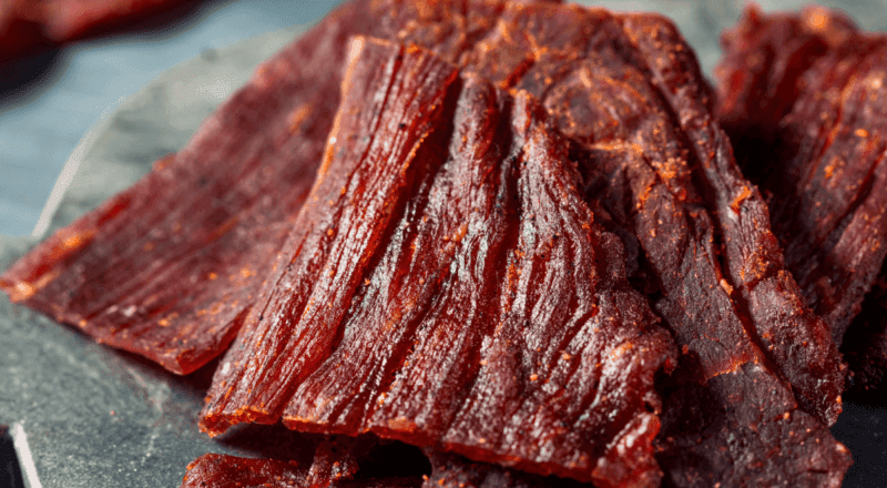 Pedaços de carne de sol sendo dessalgados em uma tigela com água, representando o processo de dessalgue ensinado no artigo.