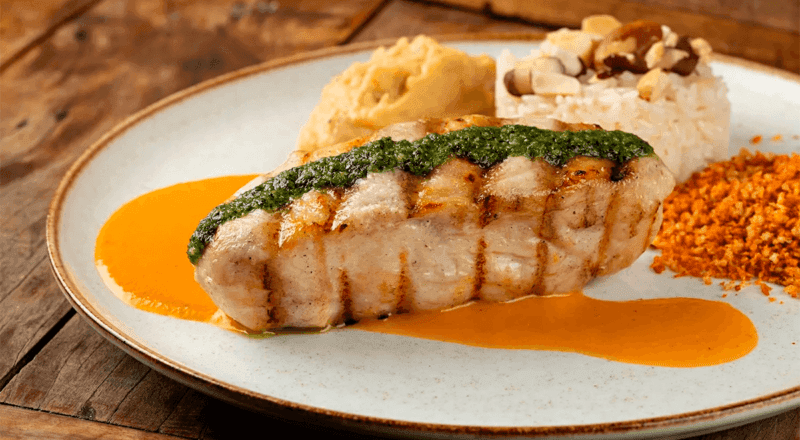 Filé de pirarucu grelhado, dourado e suculento, servido com fatias de limão e um ramo de coentro.