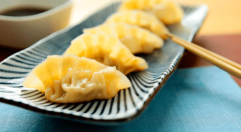 Gyozas dourados e crocantes, servidos em um prato com molho para mergulhar.