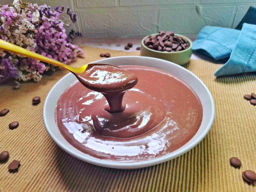 Tigela de mingau de chocolate cremoso, sem maizena, decorado com rodelas de banana e raspas de chocolate.