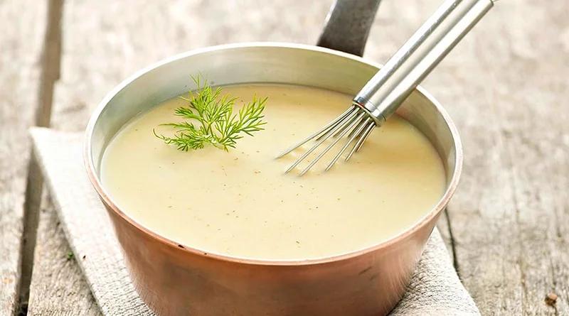 Panela grande com molho branco cremoso, sendo mexido com um fouet.