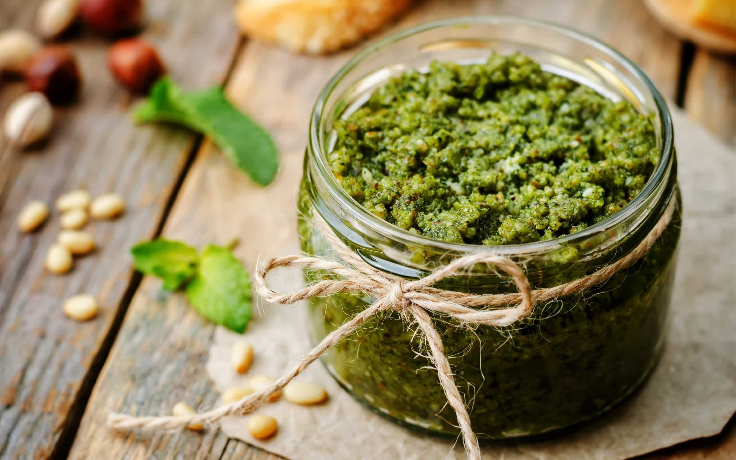 Tigela de vidro com molho pesto verde vibrante, decorado com folhas de manjericão fresco e pinoli.