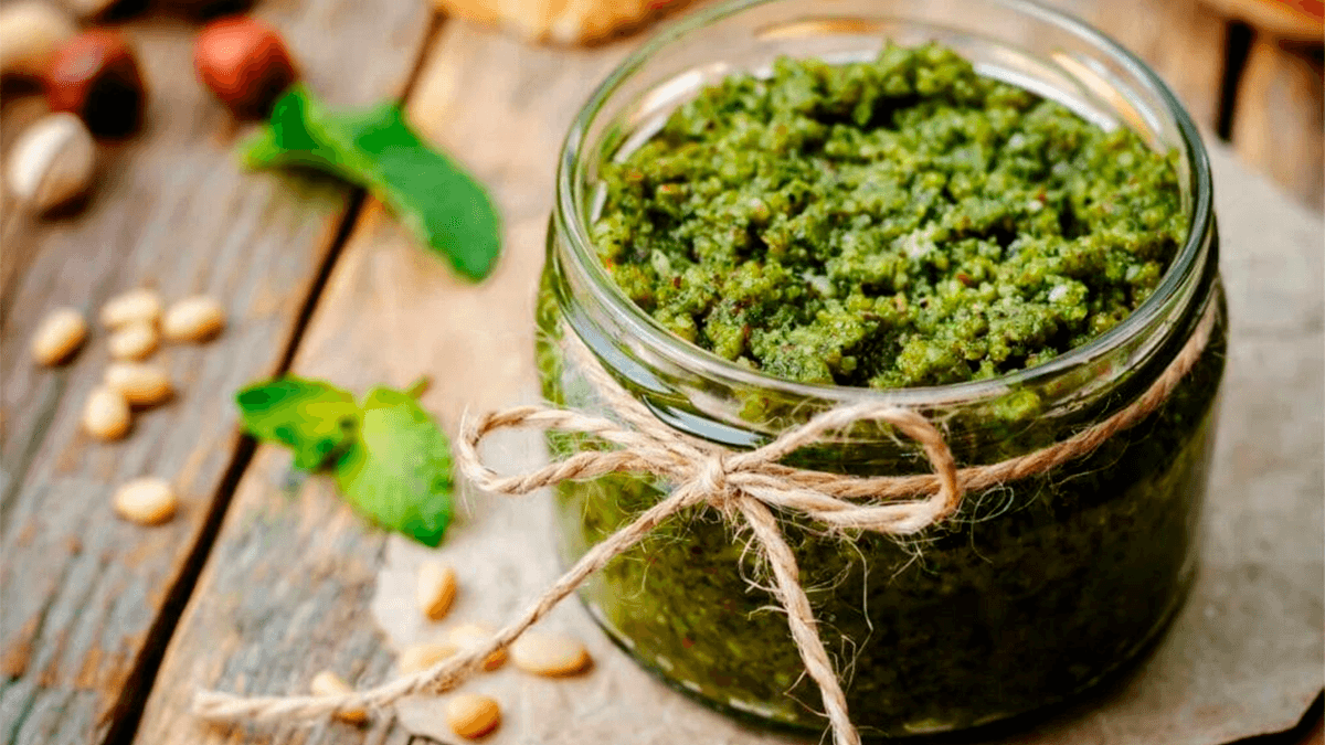 Tigela de vidro com molho pesto verde vibrante, decorado com folhas de manjericão fresco e pinoli.