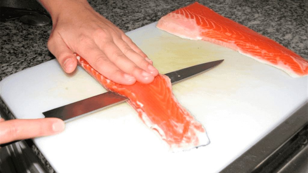 Um filé de salmão assado com a pele crocante e dourada, servido em um prato com rodelas de limão, representando o resultado final da receita e o tema do artigo.