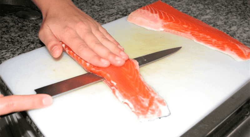 Um filé de salmão assado com a pele crocante e dourada, servido em um prato com rodelas de limão, representando o resultado final da receita e o tema do artigo.