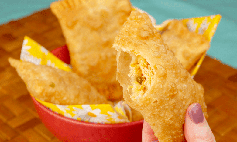 Close-up de massa de pastel de feira sendo aberta com cilindro, destacando a textura e o processo.