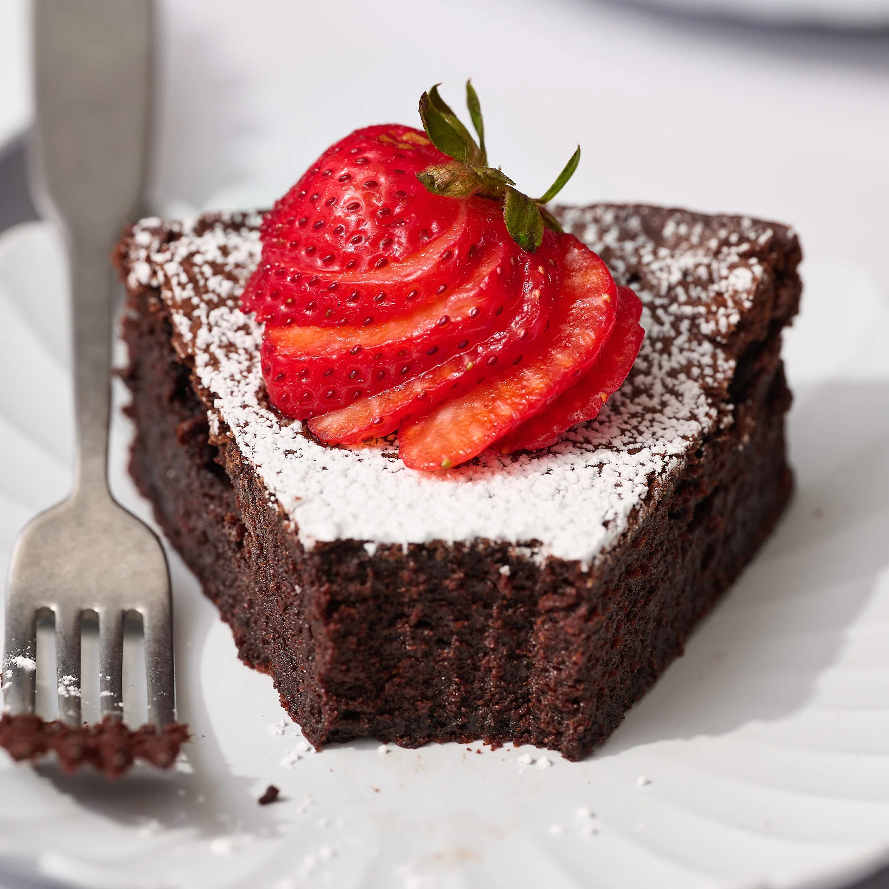 Fatia de Bolo Negro do Viena (Flourless Chocolate Cake), com textura densa e úmida, servida com framboesas frescas e uma bola de sorvete de creme.