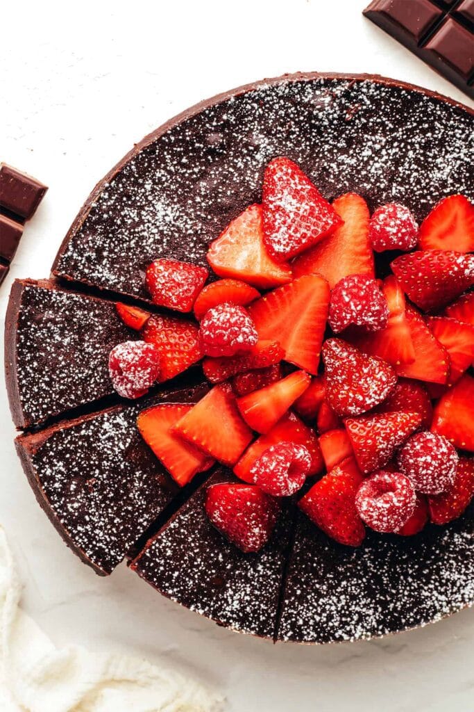 Fatia de Bolo Negro do Viena (Flourless Chocolate Cake), com textura densa e úmida, servida com framboesas frescas e uma bola de sorvete de creme.