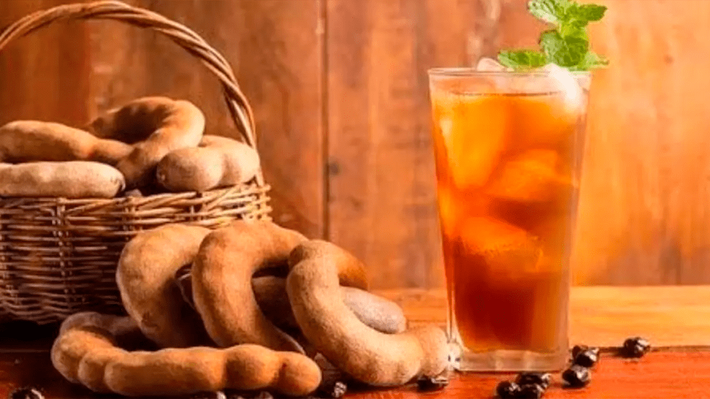 Jarra de refresco de tamarindo gelado com cubos de gelo e raminhos de hortelã, destacando a cor e a textura refrescante da bebida.