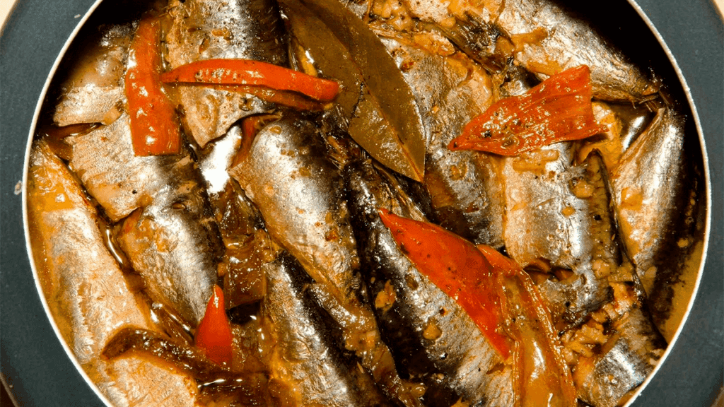 Sardinhas cozidas na panela de pressão, dispostas em um prato e cobertas com um molho, representando o resultado final da receita e o tema do artigo.