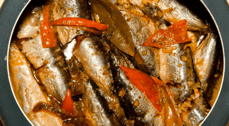 Sardinhas cozidas na panela de pressão, dispostas em um prato e cobertas com um molho, representando o resultado final da receita e o tema do artigo.