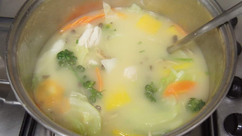 Tigela de sopa de peixe tailandesa fumegante, com pedaços de peixe branco, vegetais coloridos e cebolinha picada, em um caldo aromático.