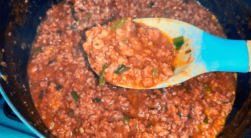 Panela com carne moída com molho, bem vermelha e suculenta, com cheiro-verde picado por cima.