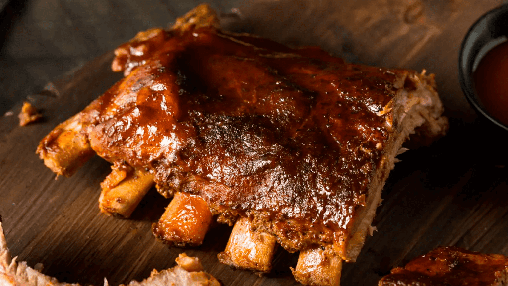 Uma costela bovina assada inteira, dourada e suculenta, saindo do forno em uma assadeira, representando o resultado final da receita e o tema do artigo.