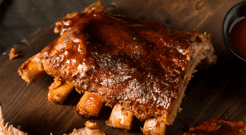 Uma costela bovina assada inteira, dourada e suculenta, saindo do forno em uma assadeira, representando o resultado final da receita e o tema do artigo.