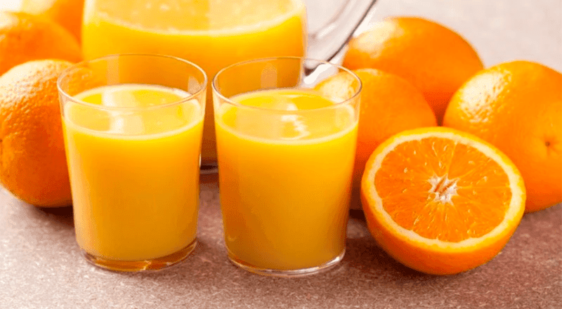 Um copo de suco de laranja fresco e vibrante, com laranjas ao fundo, representando a bebida refrescante e o tema do artigo.