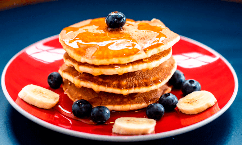 Fotografia apetitosa de uma pilha alta de panquecas americanas fofas, douradas e cobertas com frutas frescas, mel e manteiga, prontas para serem saboreadas no café da manhã.