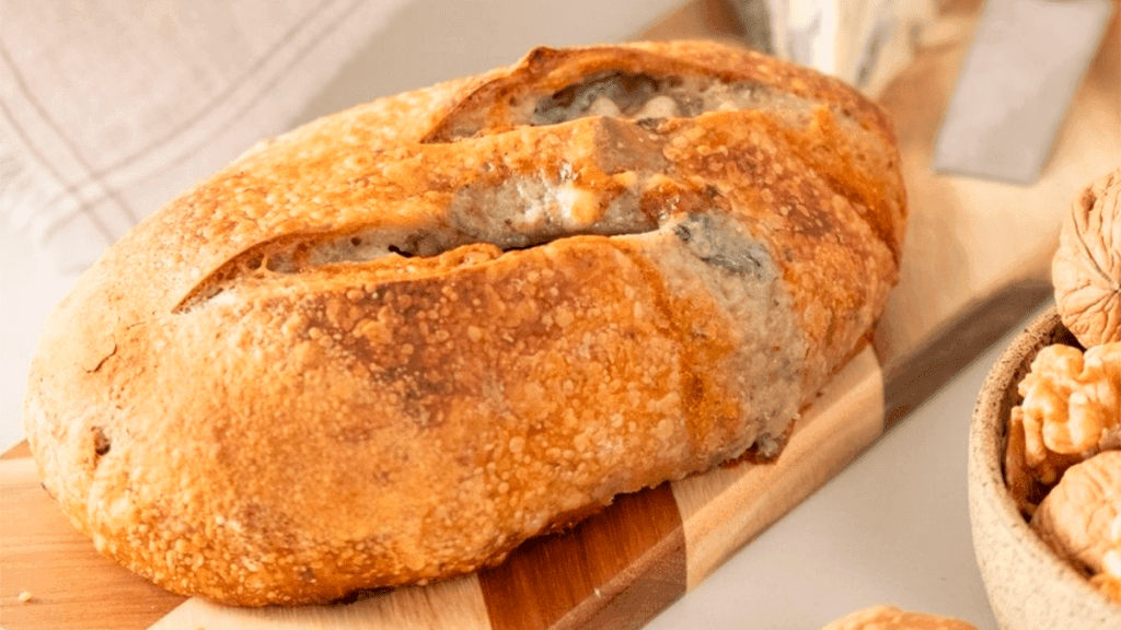 Pães de gorgonzola e nozes recém-assados, dispostos em uma cesta rústica, com queijo gorgonzola e nozes ao lado.