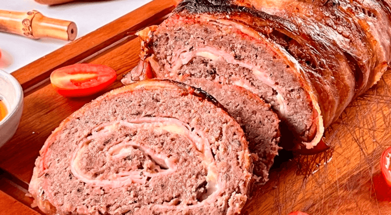 Um rocambole de carne assado e fatiado, mostrando o recheio de queijo e presunto e a suculência da carne, representando o resultado final da receita.